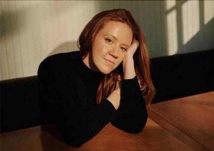 Photographer Libby Danforth sits at a table and looks directly at the camera with a slight smile.